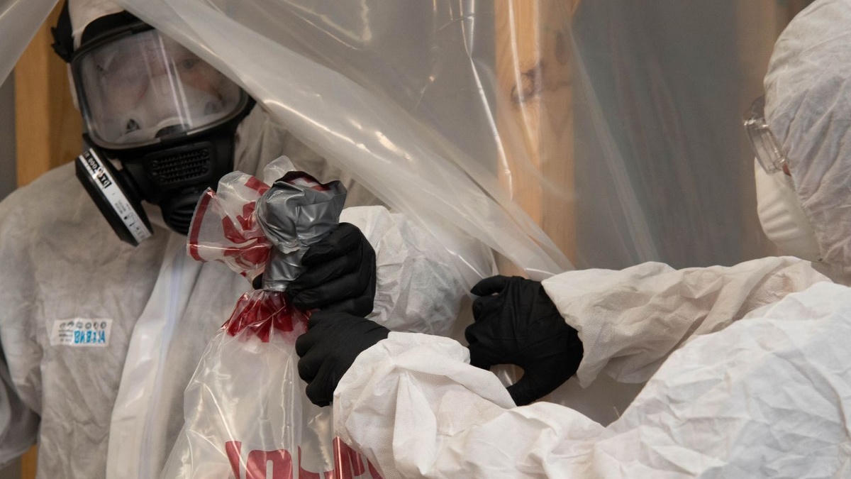 Travailleurs en combinaisons et appareils respiratoires conditionnant des déchets sous confinement